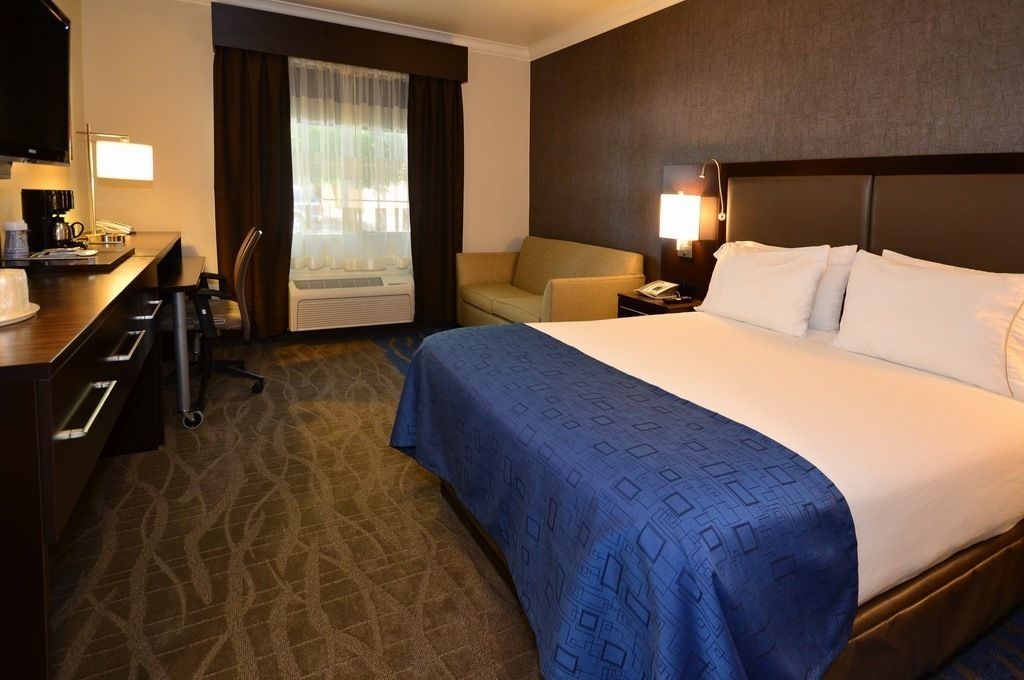 Habitación de hotel con una cama grande, un escritorio con silla, un sofá y un televisor.