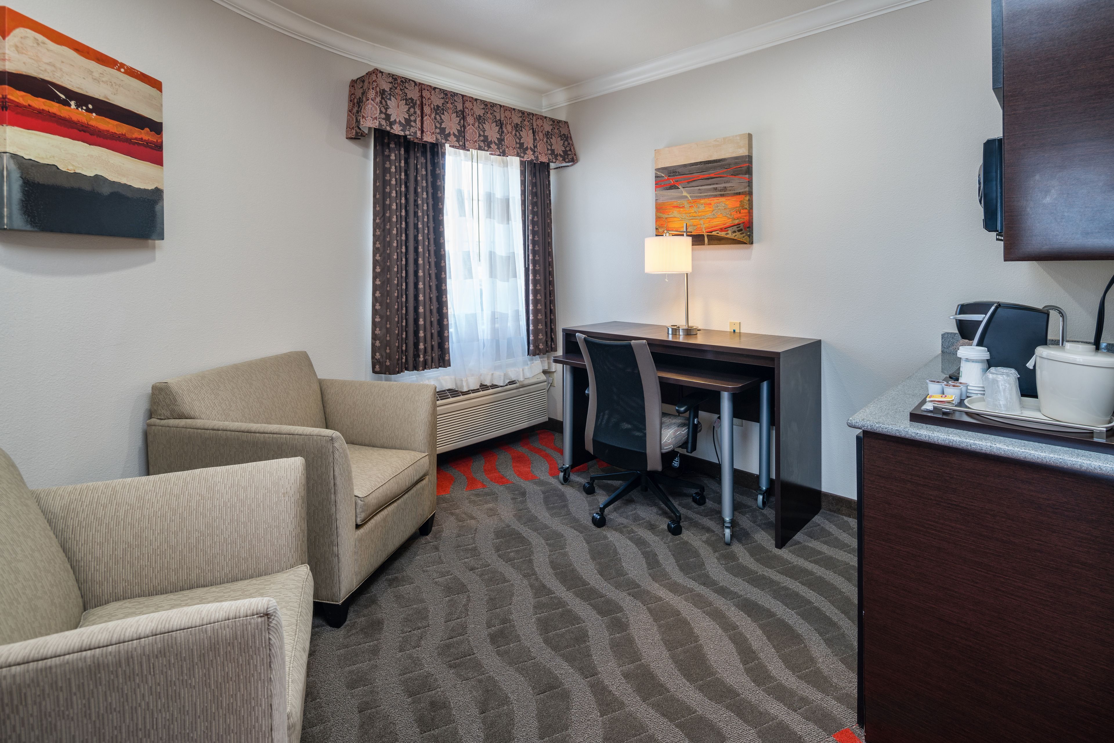 A hotel room with a sofa, a desk, a lamp, and a painting on the wall.