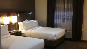 Habitación de hotel con dos camas, una mesita de noche con lámparas, una ventana con cortinas y un aire acondicionado instalado en la pared.