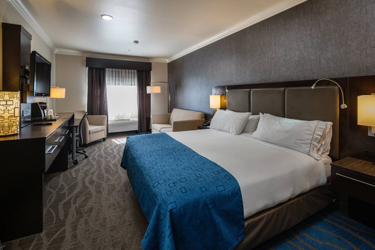 Une chambre d’hôtel avec un grand lit, un bureau, une chaise, une télévision et une fenêtre avec des rideaux.