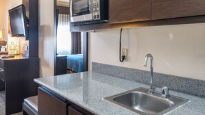 A modern kitchen with dark wood cabinets, a granite countertop, a stainless steel sink, and a microwave.