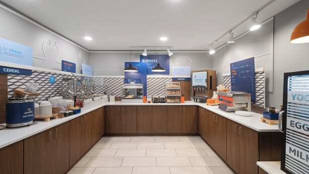 A modern breakfast area with a counter, display signs, and a digital menu board. - Holiday Inn Exp Winston Salem by IHG (Winston-Salem)