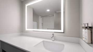 A modern bathroom with a white sink, a large mirror with integrated lighting, and a shower area visible in the background.
