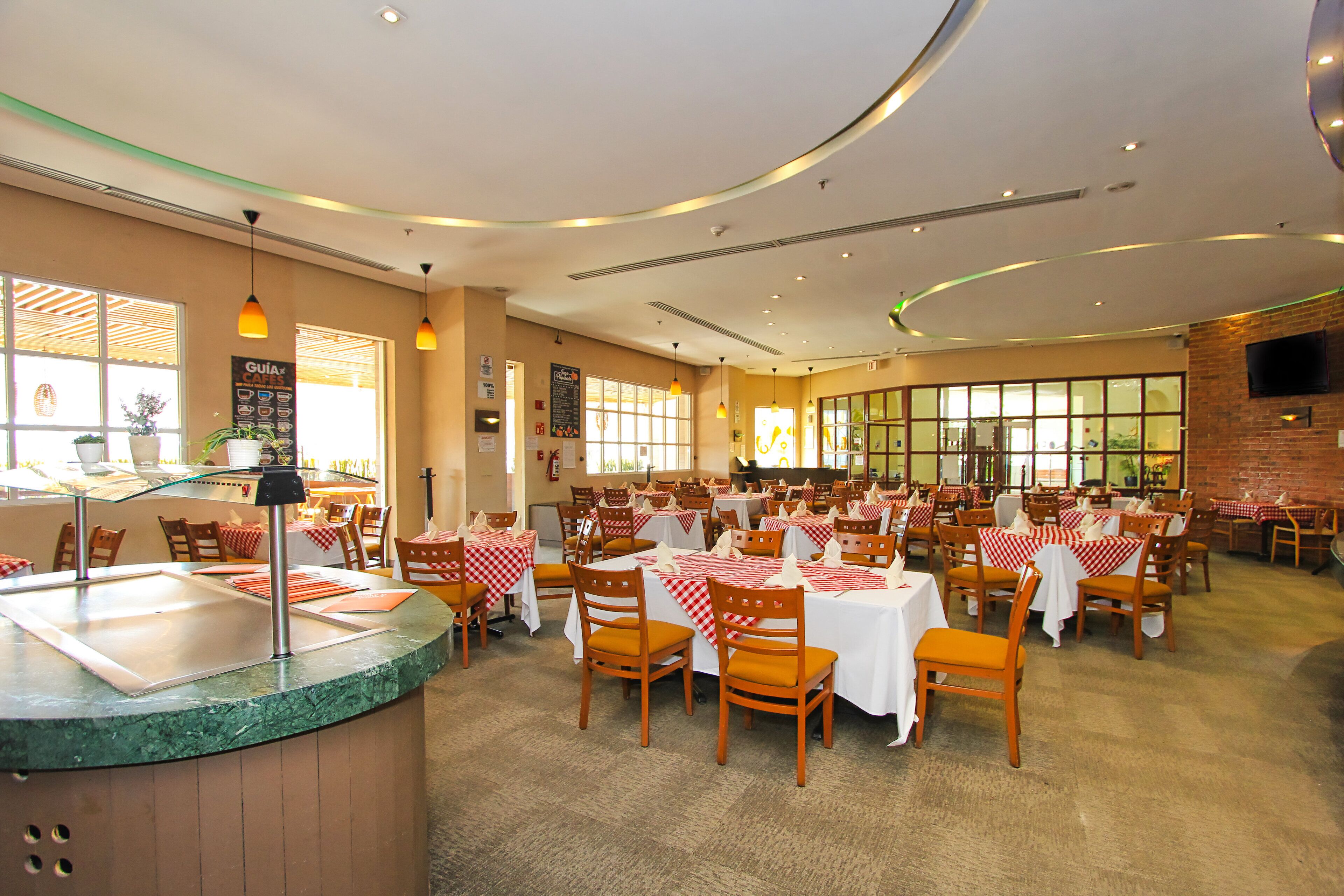 A spacious restaurant with multiple tables and chairs, a counter area, and large windows allowing natural light.