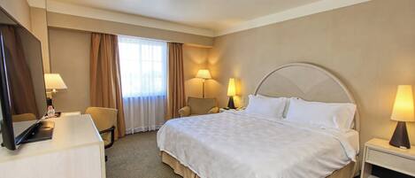 Une chambre d’hôtel avec un grand lit, deux lampes de chevet, un bureau avec un ordinateur et une chaise.