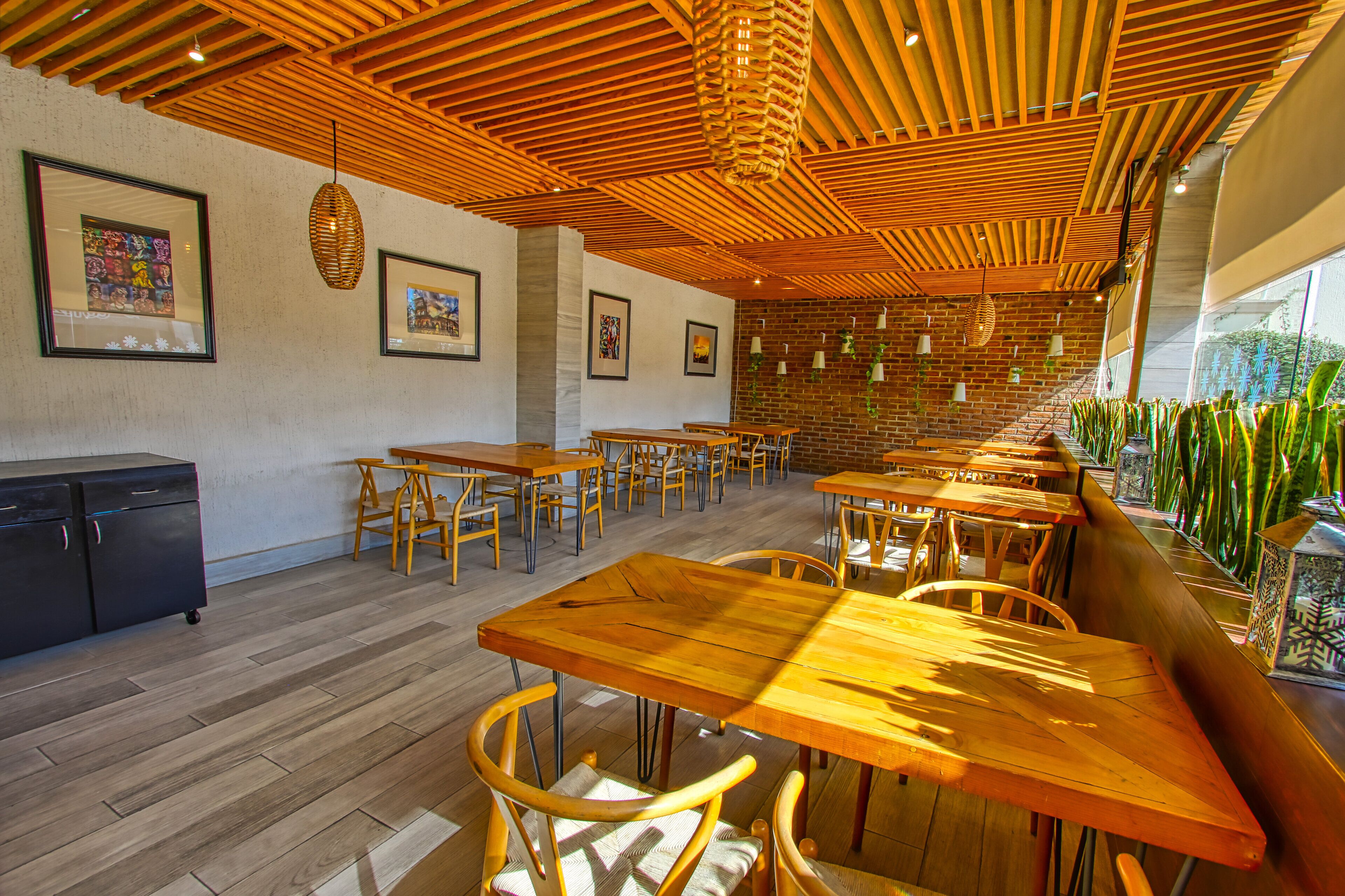 A restaurant with wooden tables and chairs, a brick wall, and framed artwork on the walls.