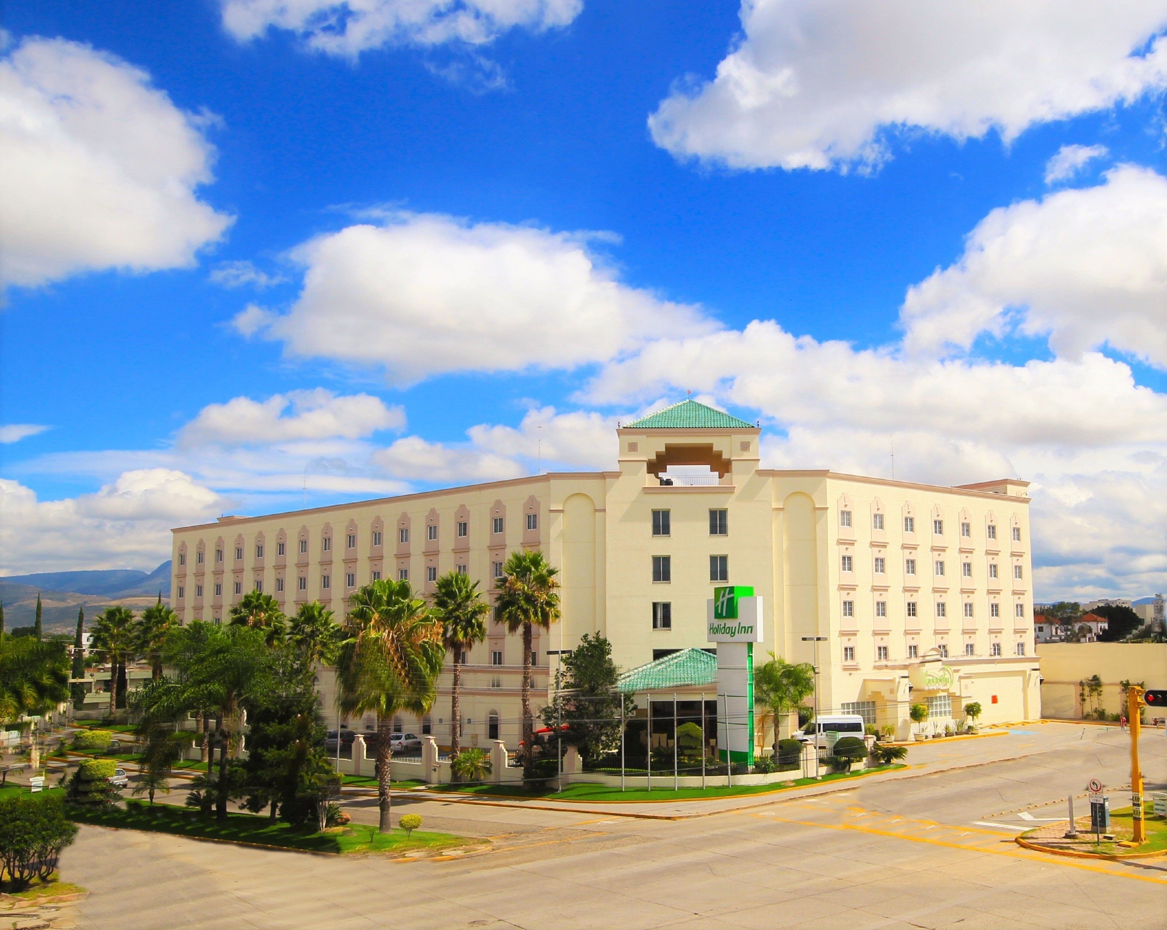 Un hotel grande con una torre central, varios pisos y una entrada verde.