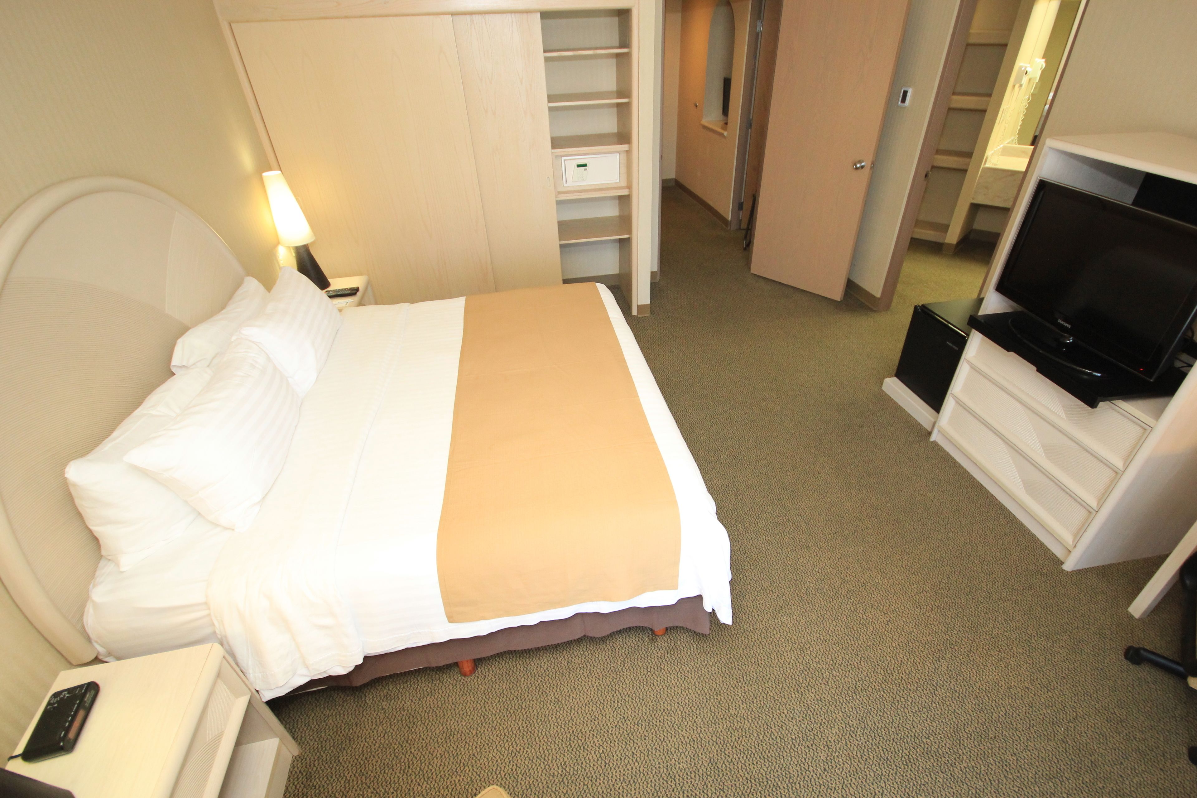 A hotel room with a bed, a TV, a desk with a lamp, and a closet.