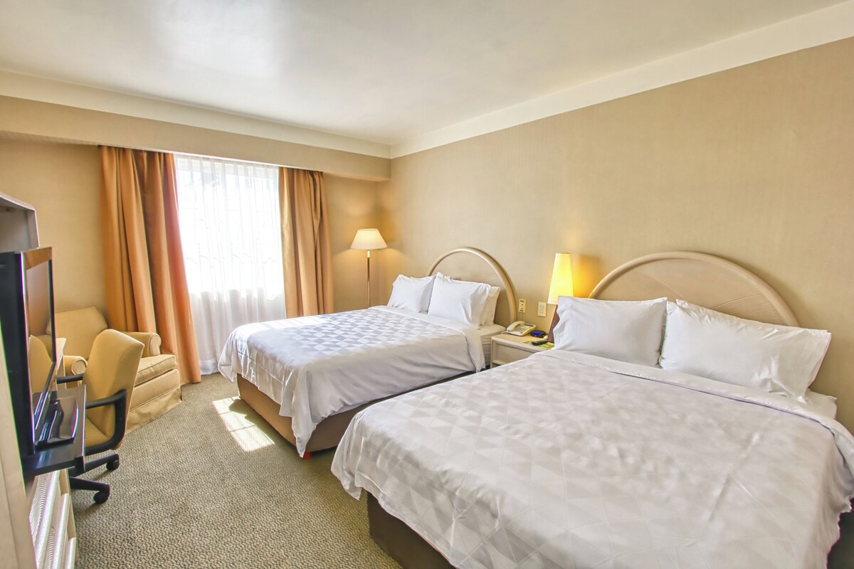 Habitación de hotel con dos camas, un escritorio, una silla y un televisor.