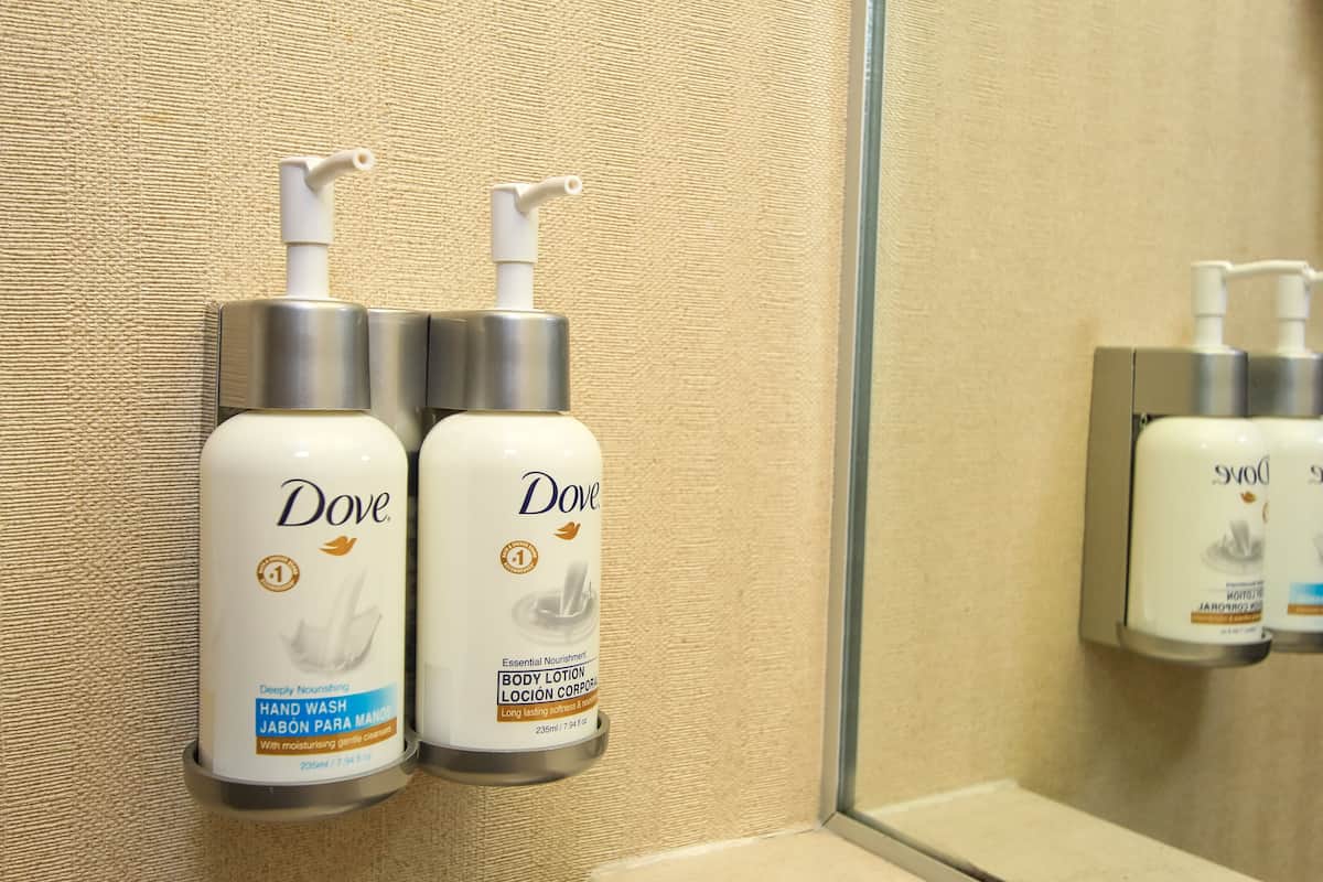 Dove hand wash and body lotion dispensers mounted on a beige textured wall in a bathroom.