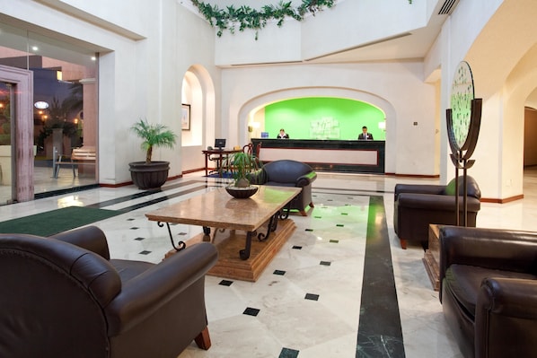 Un vestíbulo con mostrador de recepción, asientos de cuero, una mesa de centro y una pared verde.