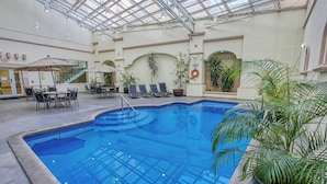 Una piscina interior con techo de cristal, rodeada de sillones de descanso y plantas en macetas.