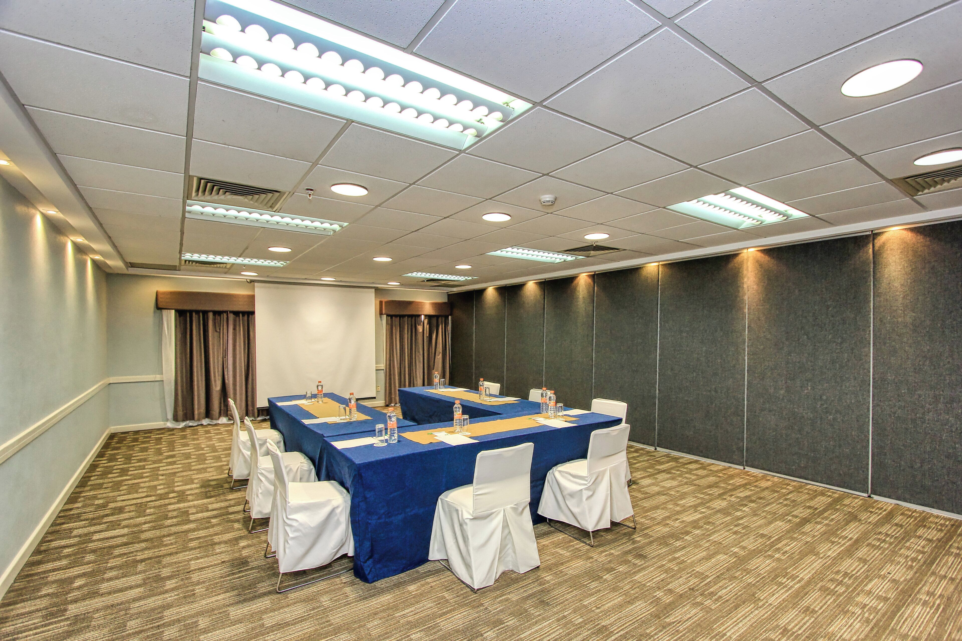 A conference room with a long table, white chairs, and a projector screen.