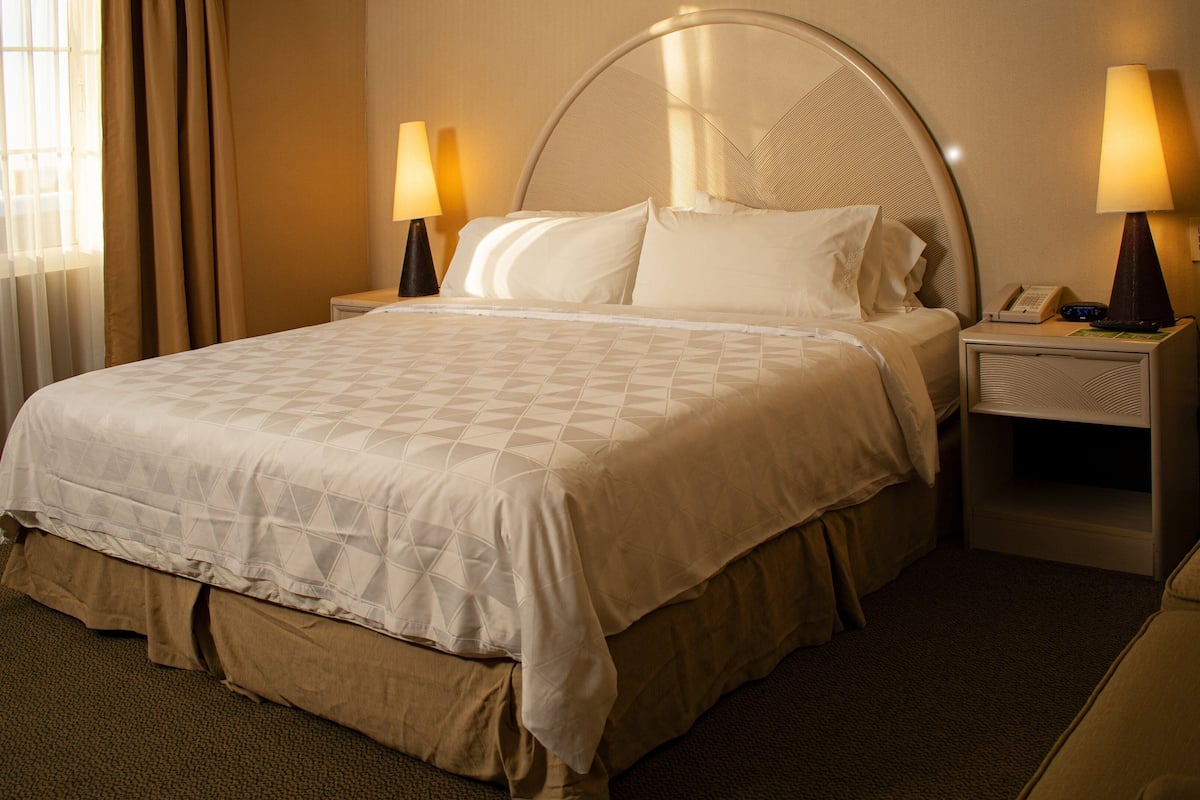 A hotel room with a large bed, two bedside tables, a lamp on each table, and a window with curtains.