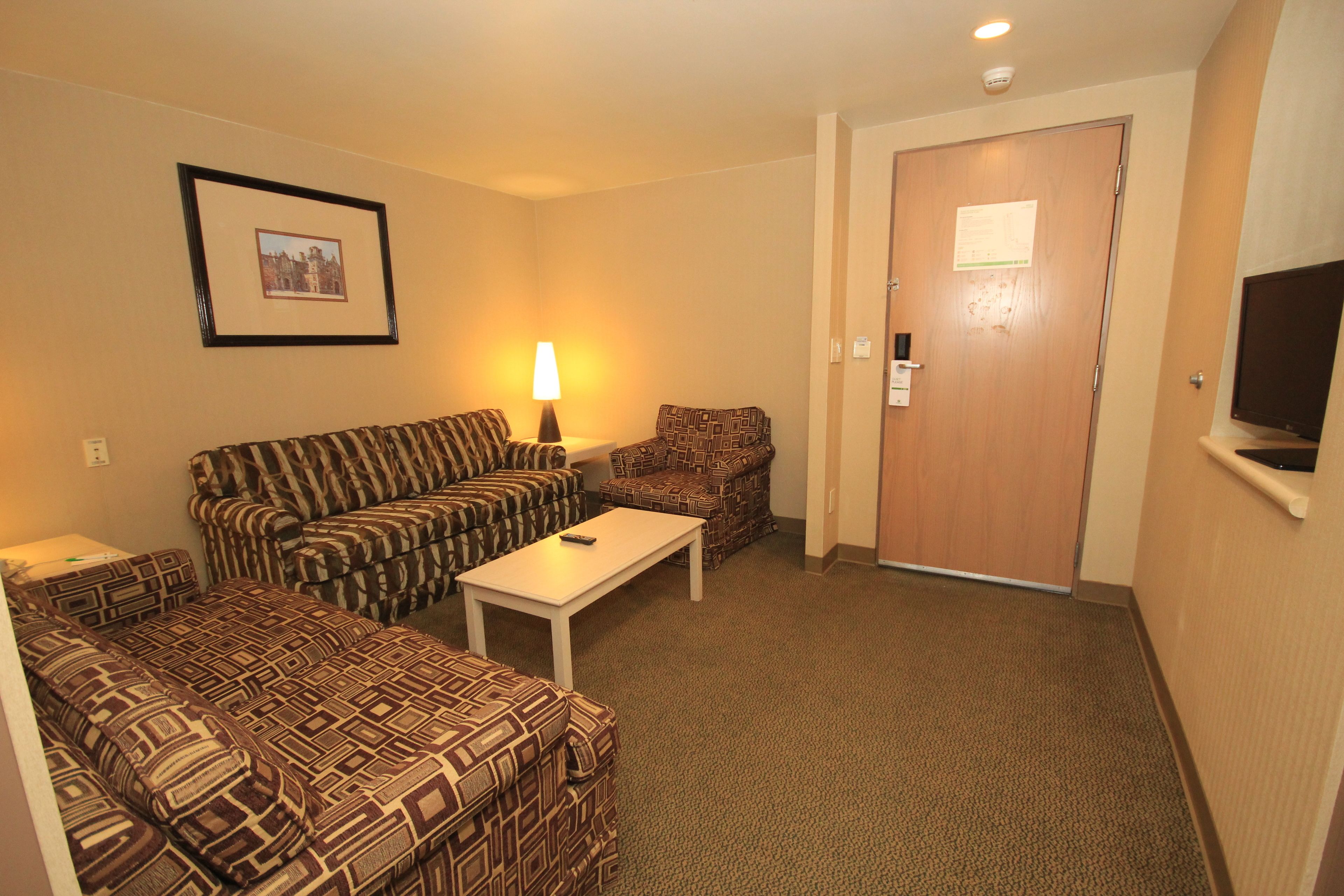 Habitación de hotel con sillones estampados, una mesita, televisión y una puerta con un letrero.