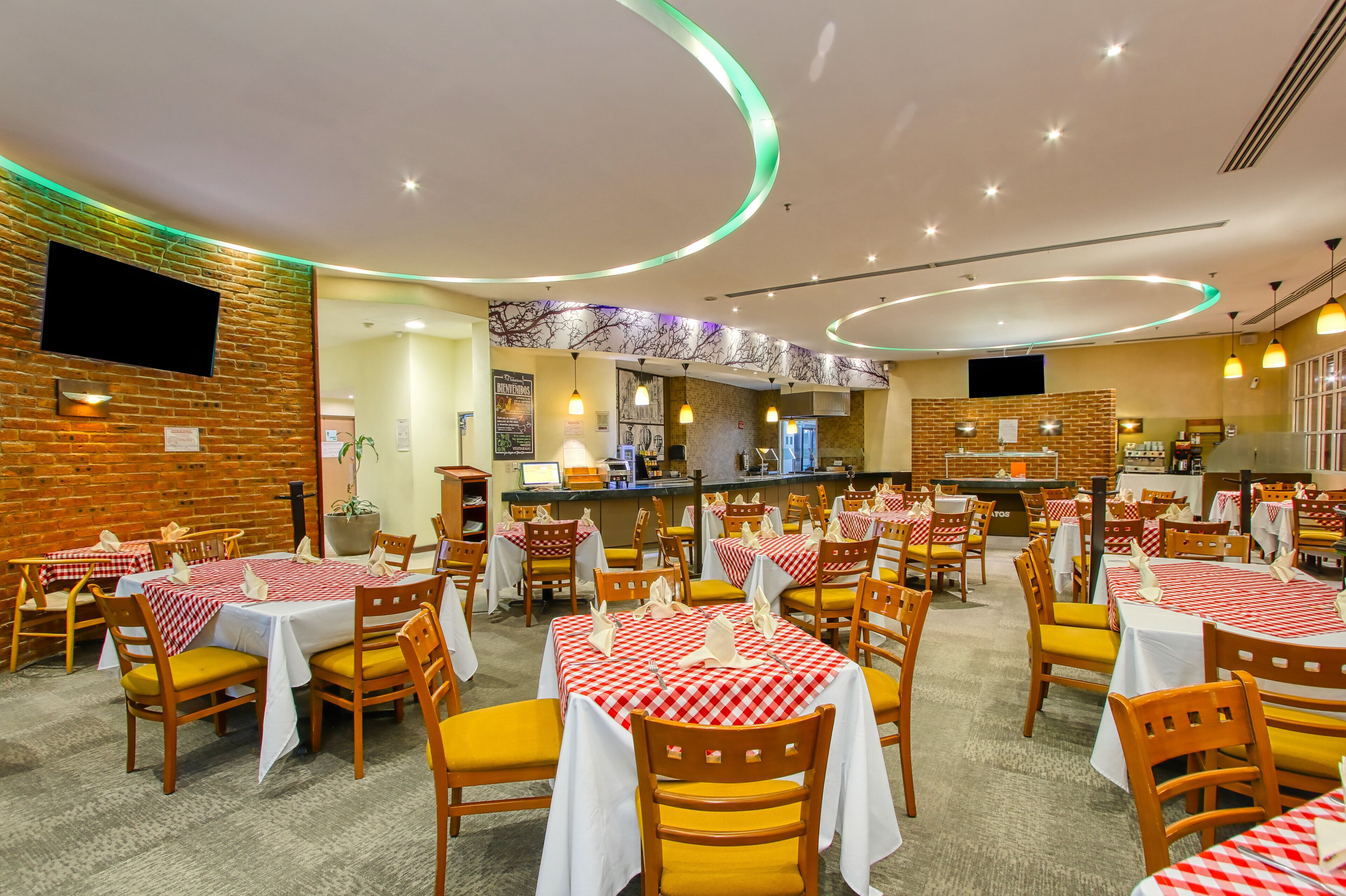 A restaurant with multiple tables and chairs, a counter, and a brick wall.