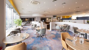 A modern hotel lobby with multiple seating areas, a bar, and a visible kitchen area.