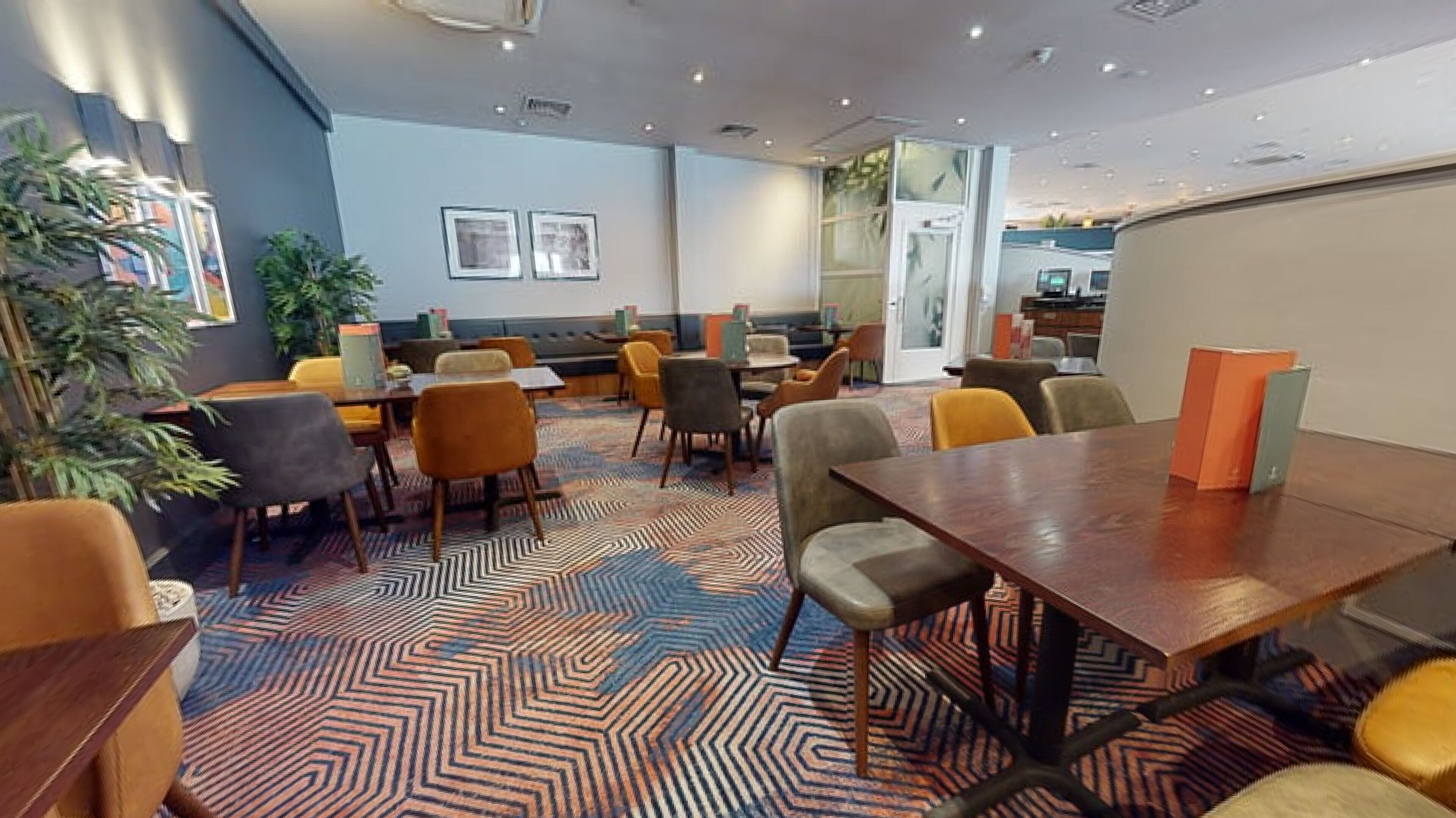 Un espace de restauration moderne, doté de plusieurs tables et chaises, d’un tapis à motifs et d’œuvres d’art accrochées aux murs.