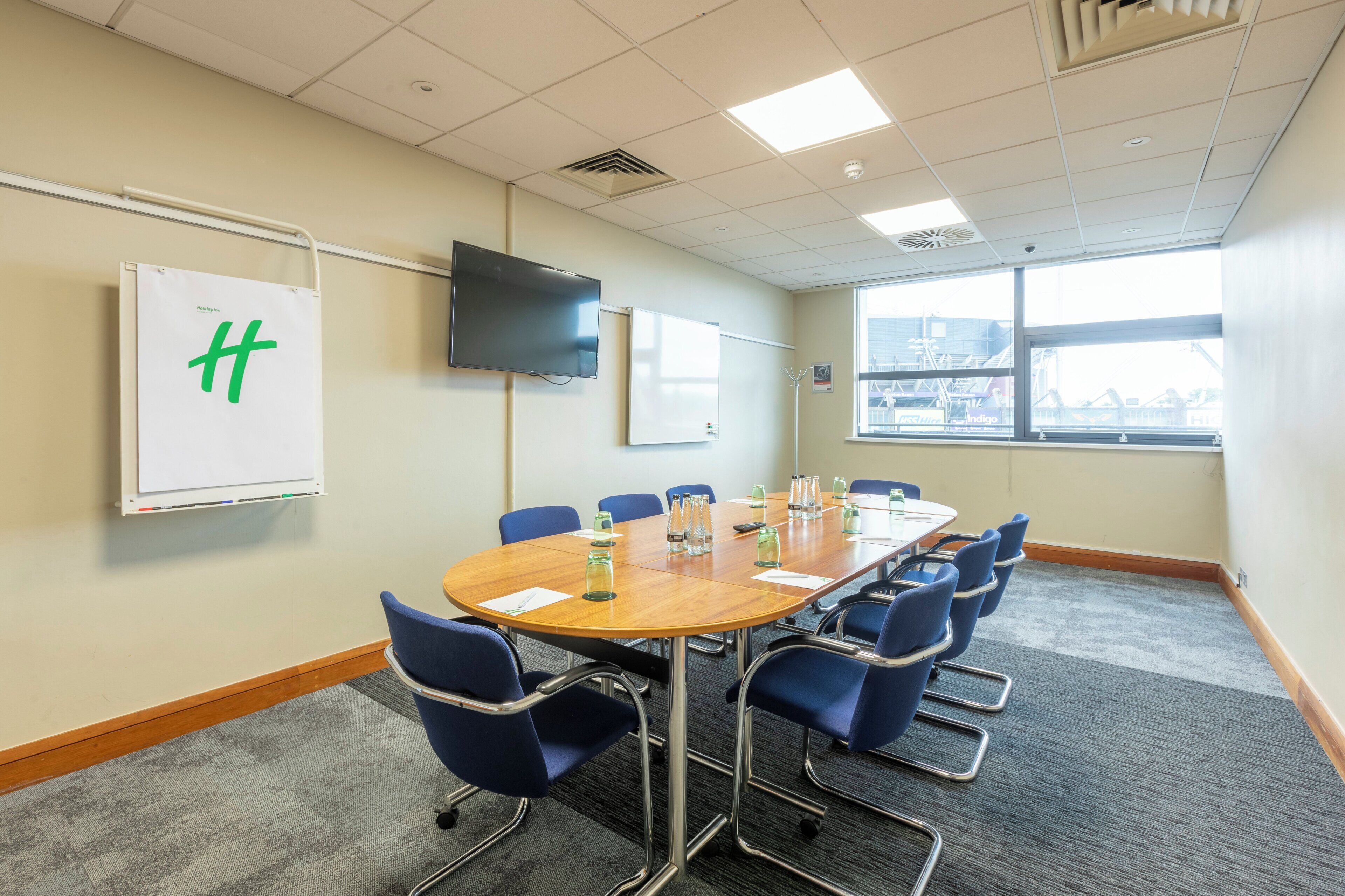A conference room with a large table, blue chairs, a whiteboard, and a flat-screen TV.