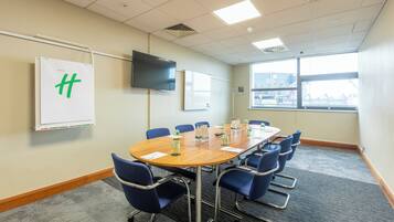 A conference room with a large table, blue chairs, a whiteboard, and a flat-screen TV.