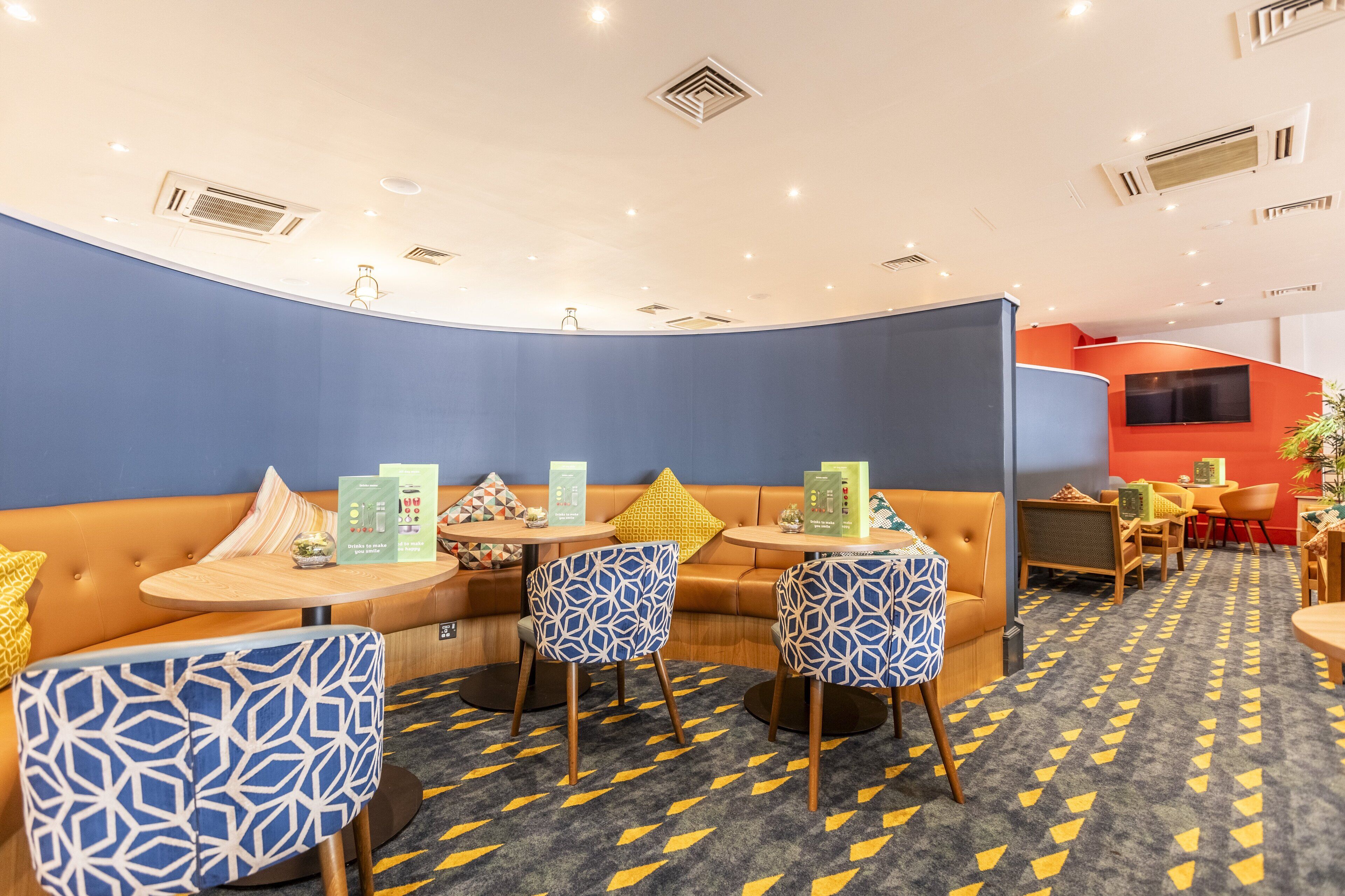 Un área de lounge moderna con una disposición de asientos curva, mesas con menús y sillas estampadas.