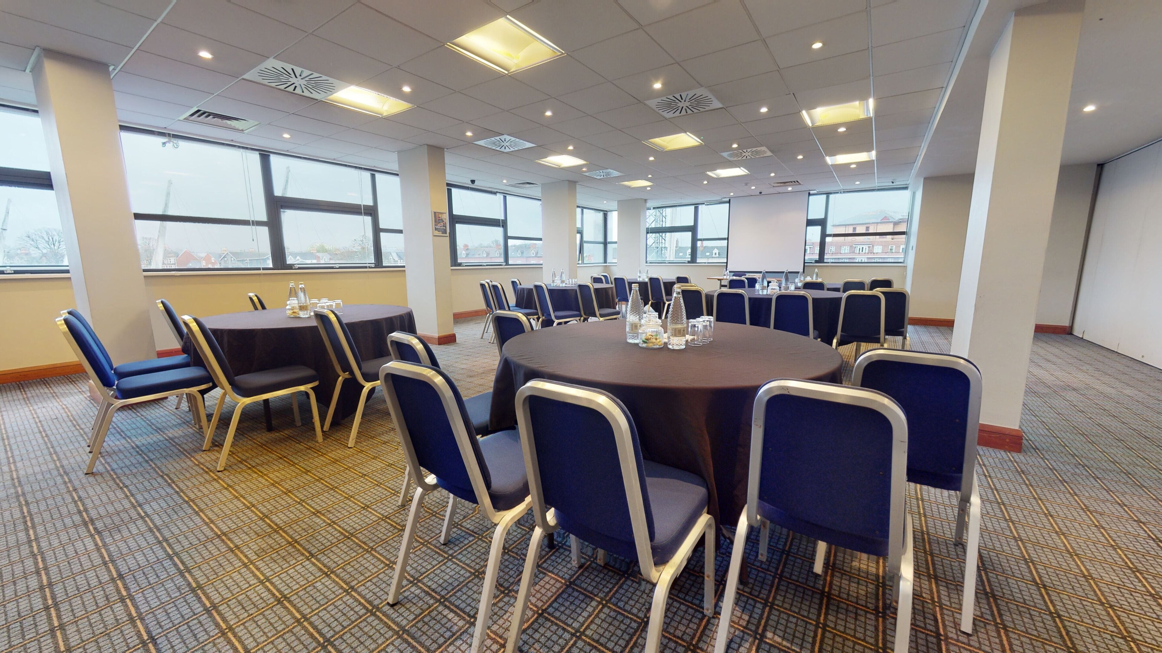 A conference room with round tables, chairs, and a carpeted floor.