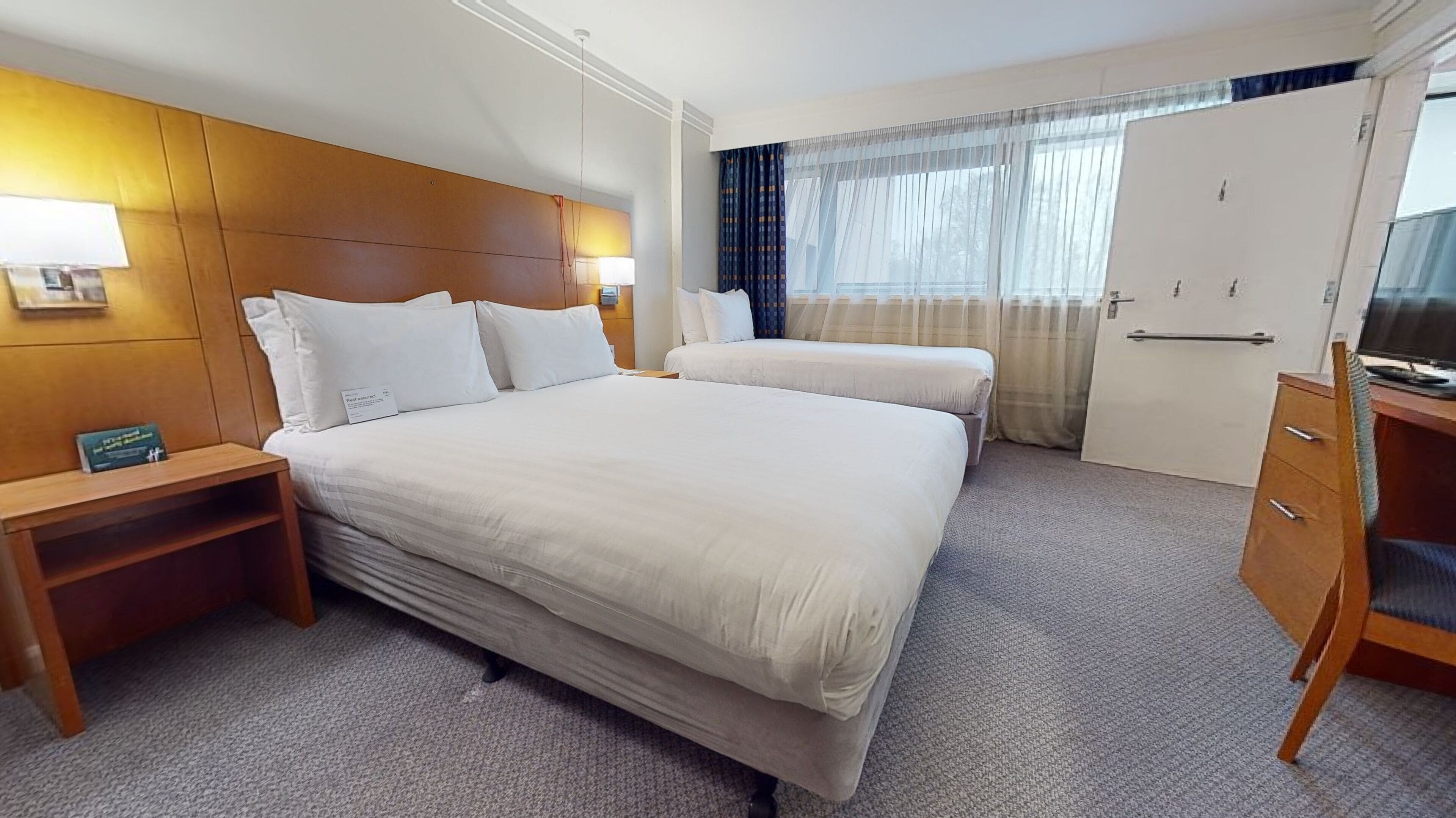 A hotel room with a large bed, bedside tables, a TV, and a wardrobe.