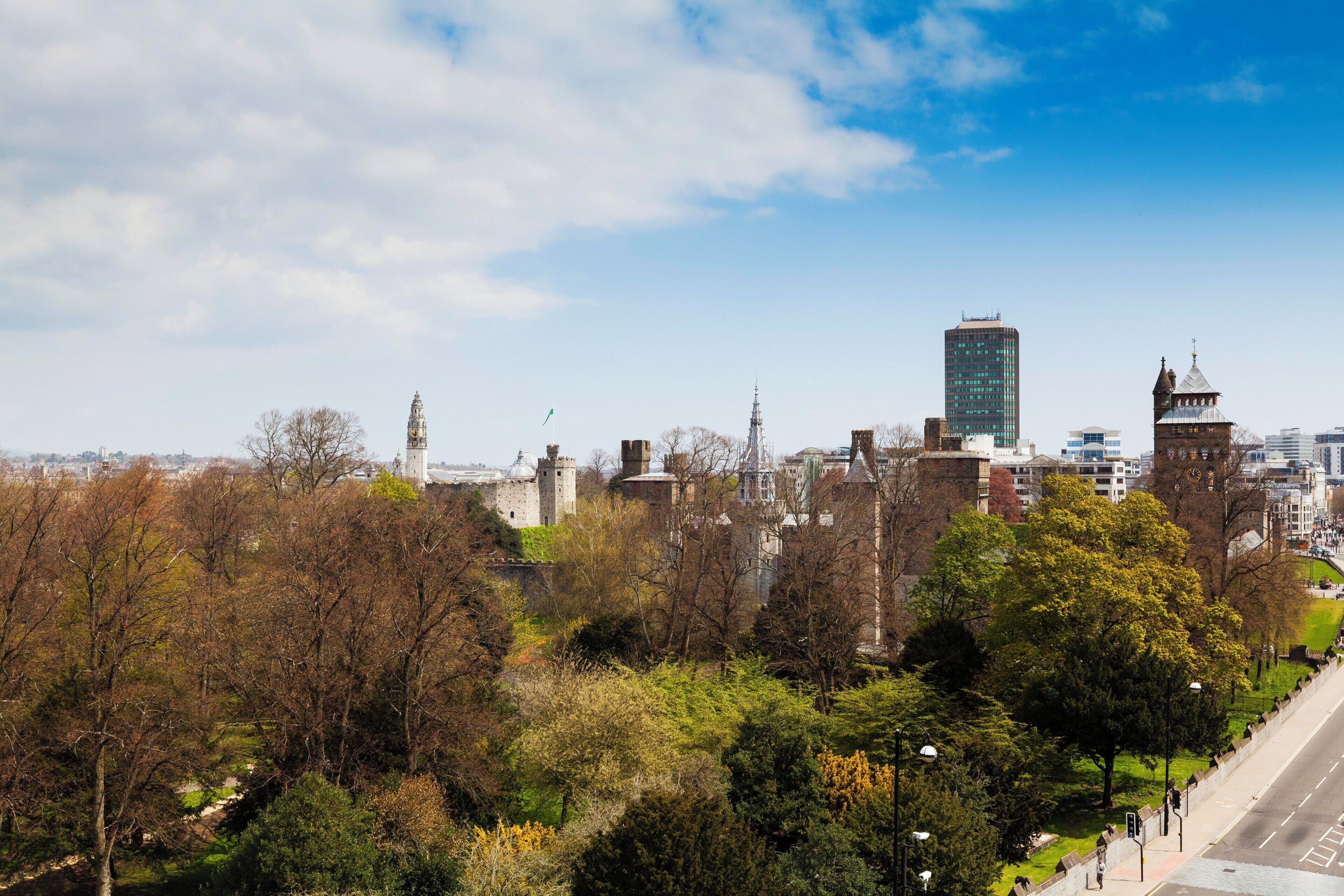 A cityscape with historic buildings, modern skyscrapers, and a park with trees.