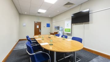 A conference room with a long table, blue chairs, a flat-screen TV, and a welcome sign.