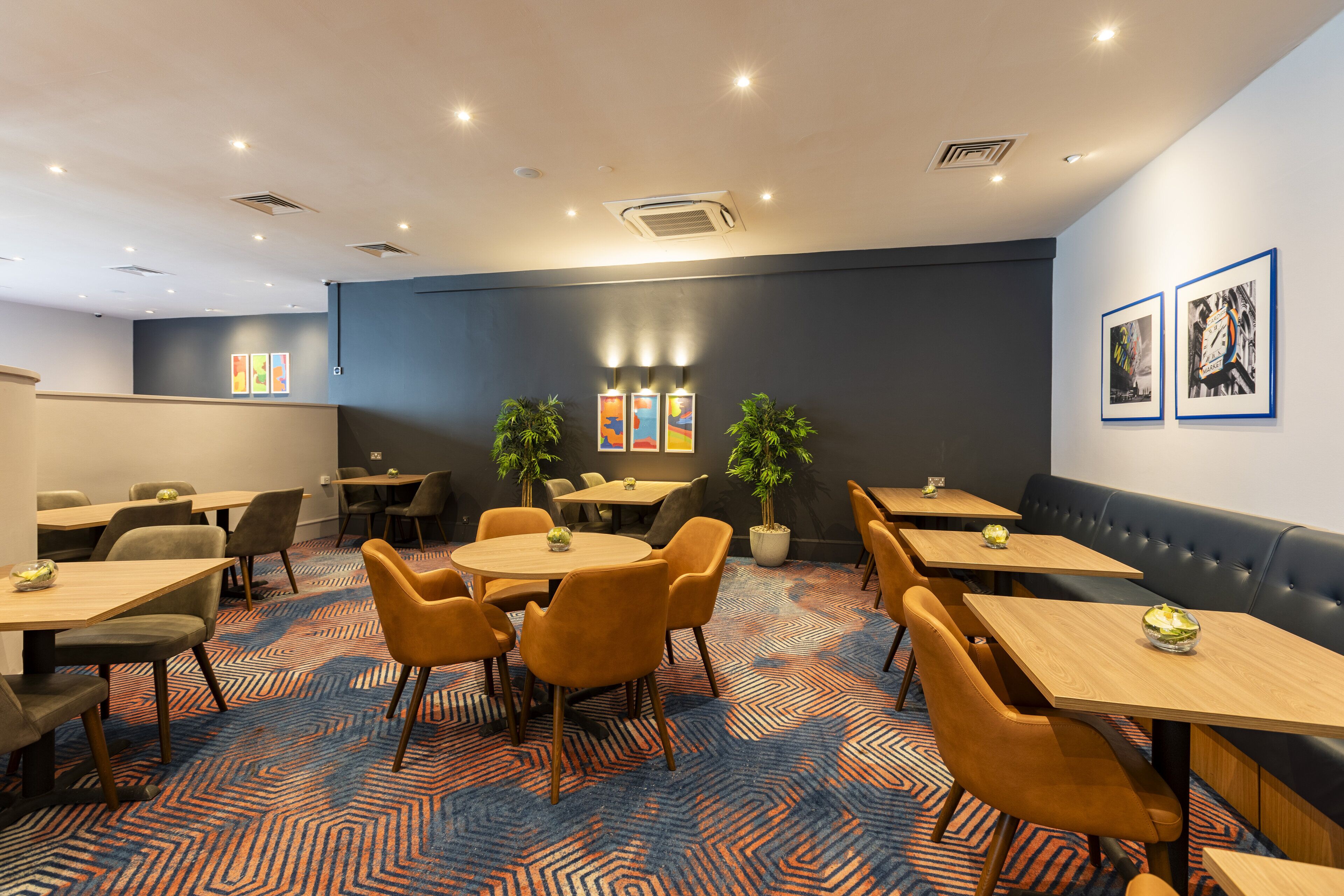 Un comedor moderno con mesas redondas, sillas anaranjadas y una alfombra estampada.