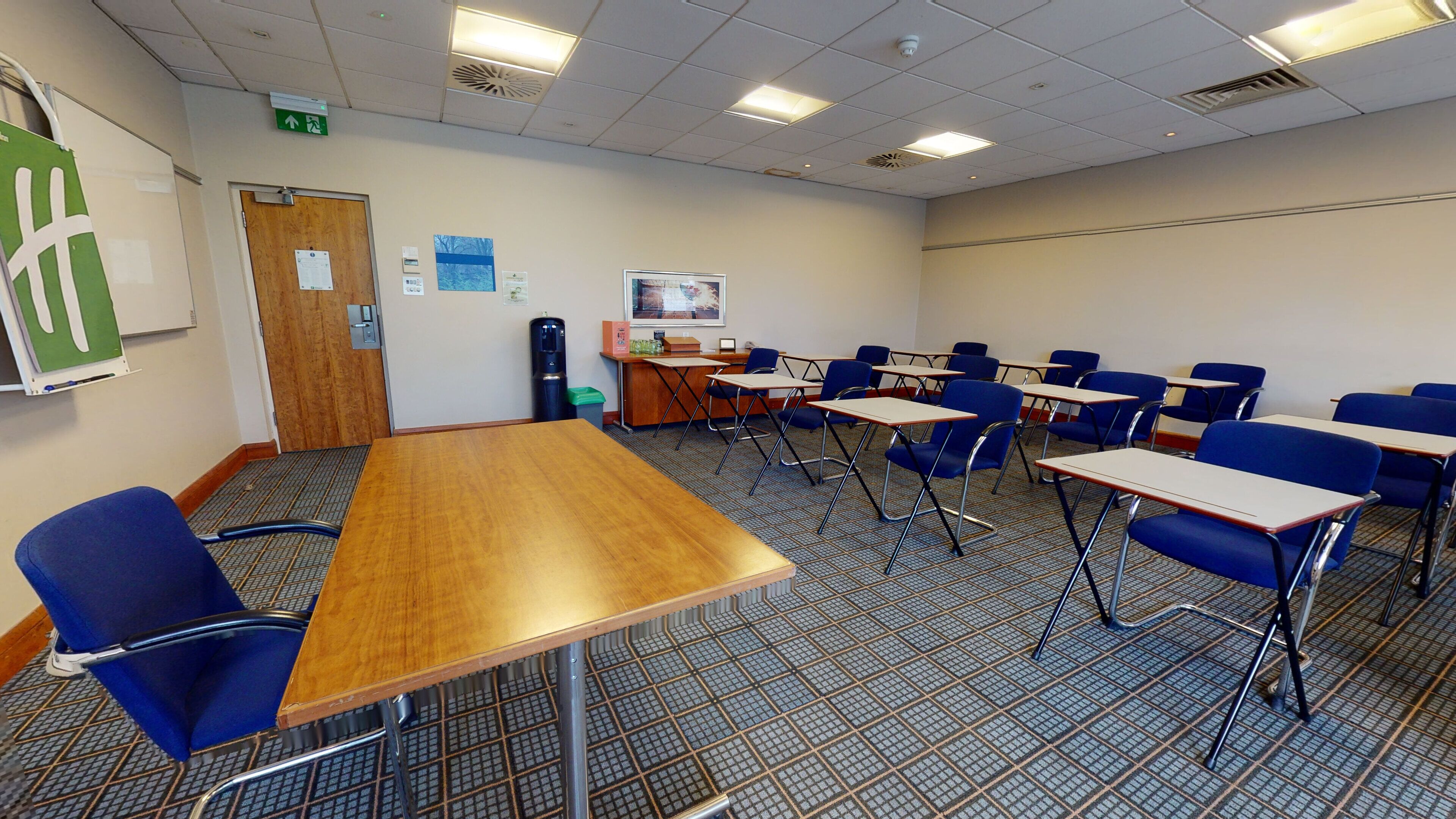 Une salle de conférence avec une longue table, des chaises bleues, un distributeur d’eau et un tableau d’affichage où sont accrochées des annonces.
