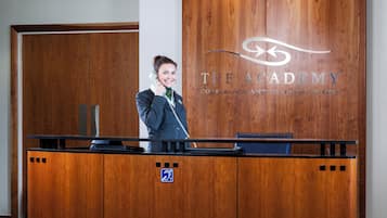 Een receptiebalie met houten afwerking, een logo voor 'The Academy Conference and Training Suites', en een blauw toegankelijkheidsbord.