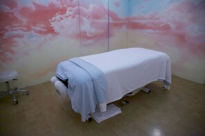 Una sala clínica con una cama, un taburete pequeño y un mural en la pared.