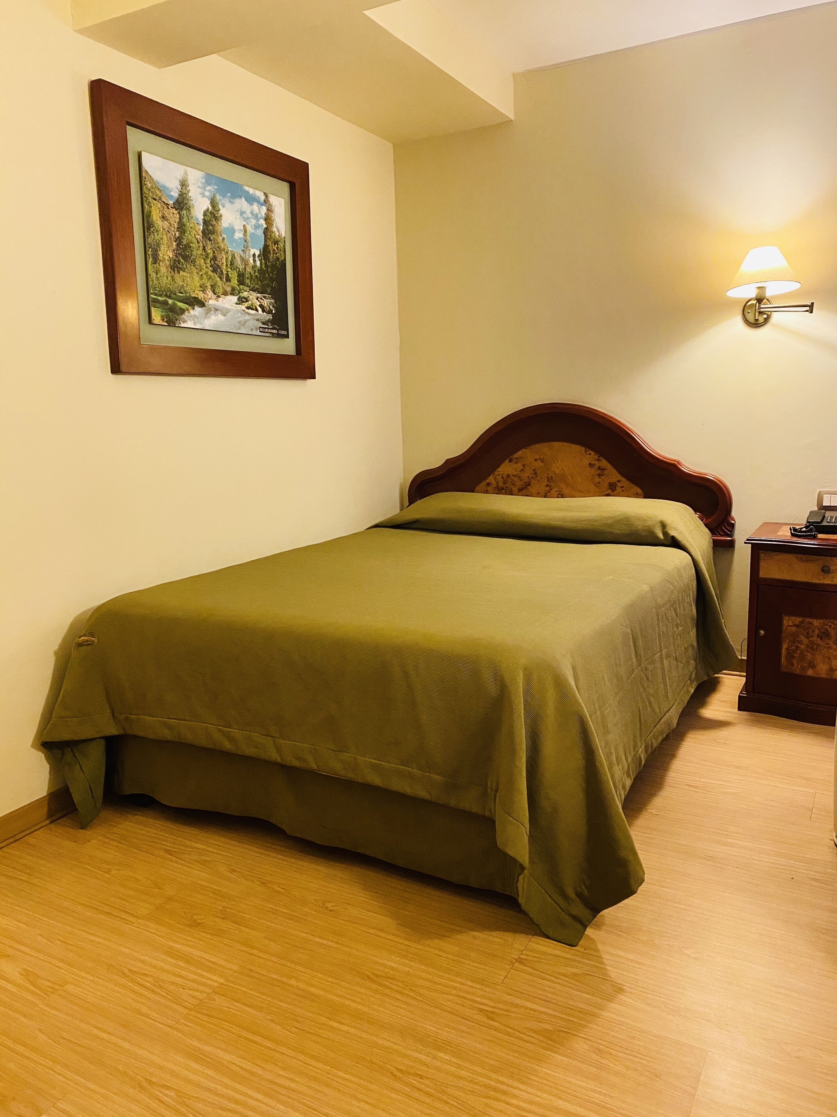 Un lit simple avec une tête de lit en bois et une couvre-lit verte, dans une pièce dont le sol est en bois.