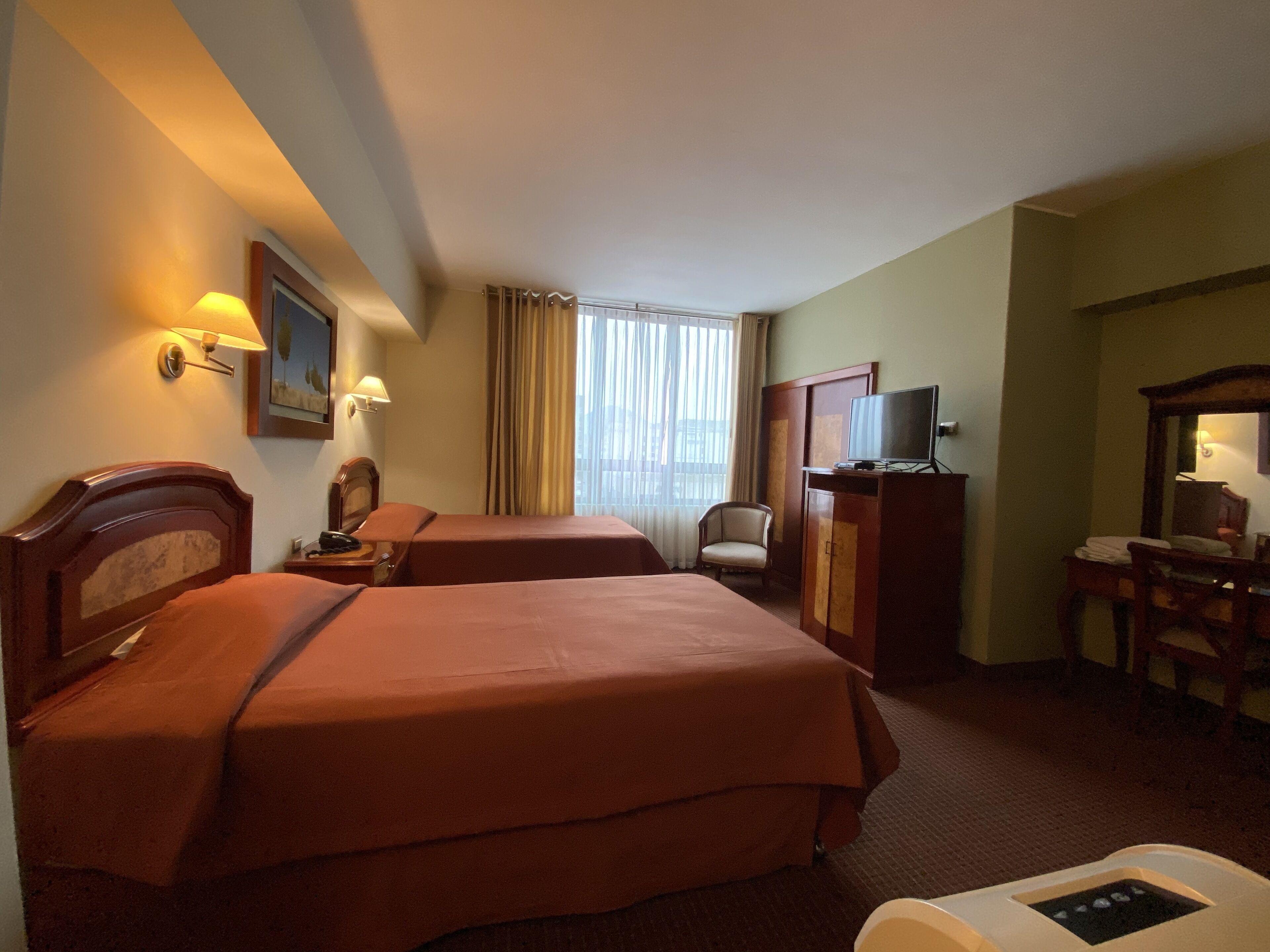A hotel room with two beds, a desk, a chair, a television, and a window with curtains.