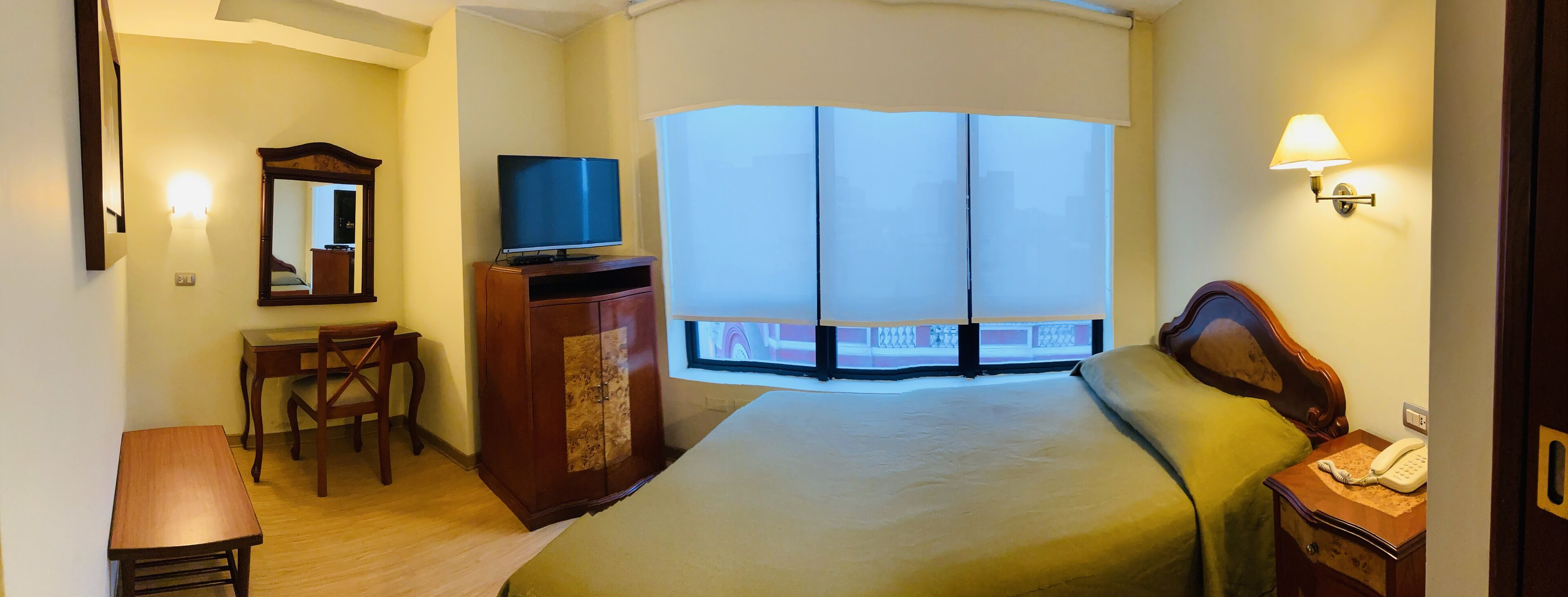 Hotelkamer met een bed, een bureau met stoel, een televisie, een kledingkast, een nachtkastje met lamp en een raam met uitzicht.