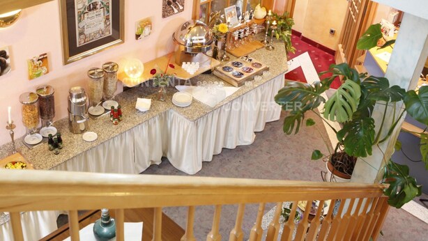 A well-decorated buffet table with various food items and condiments, set in a room with a staircase and potted plants. - Bebras Hessischer Hof (Bebra)