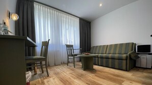 A modern living room with a wooden floor, a sofa, two chairs, a small table, and a kitchenette area. - Bebras Hessischer Hof (Bebra)