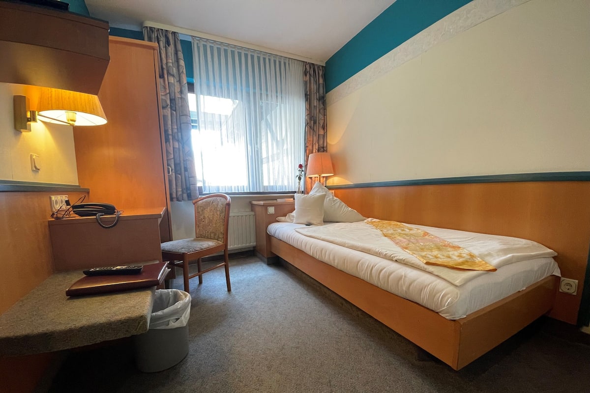 A hotel room with a bed, a desk, a chair, a telephone, and a window with curtains.