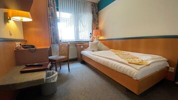 A hotel room with a bed, a desk, a chair, a telephone, and a window with curtains.