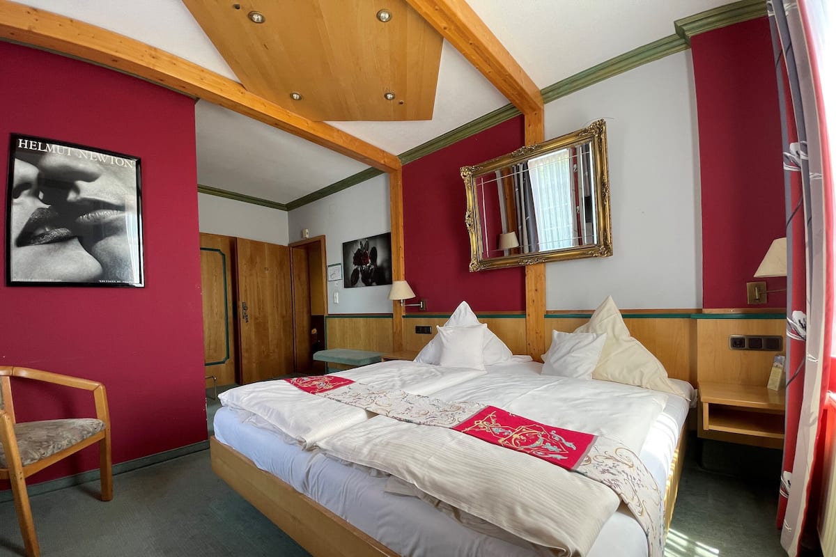 A hotel room with a large bed, wooden headboard, red walls, and a framed mirror.