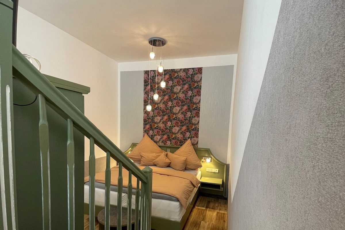 A staircase leading to a bedroom with a bed, a nightstand, and a wall with floral wallpaper.