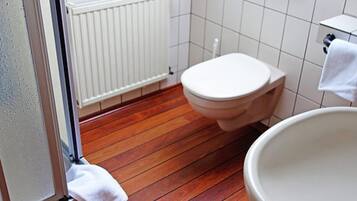 Et badeværelse med trægulv, hvide fliser, et hvidt toilet og en vask.