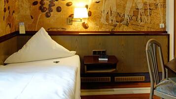 A hotel room with a bed, a nightstand with a lamp, a chair, and a wall with a map design.