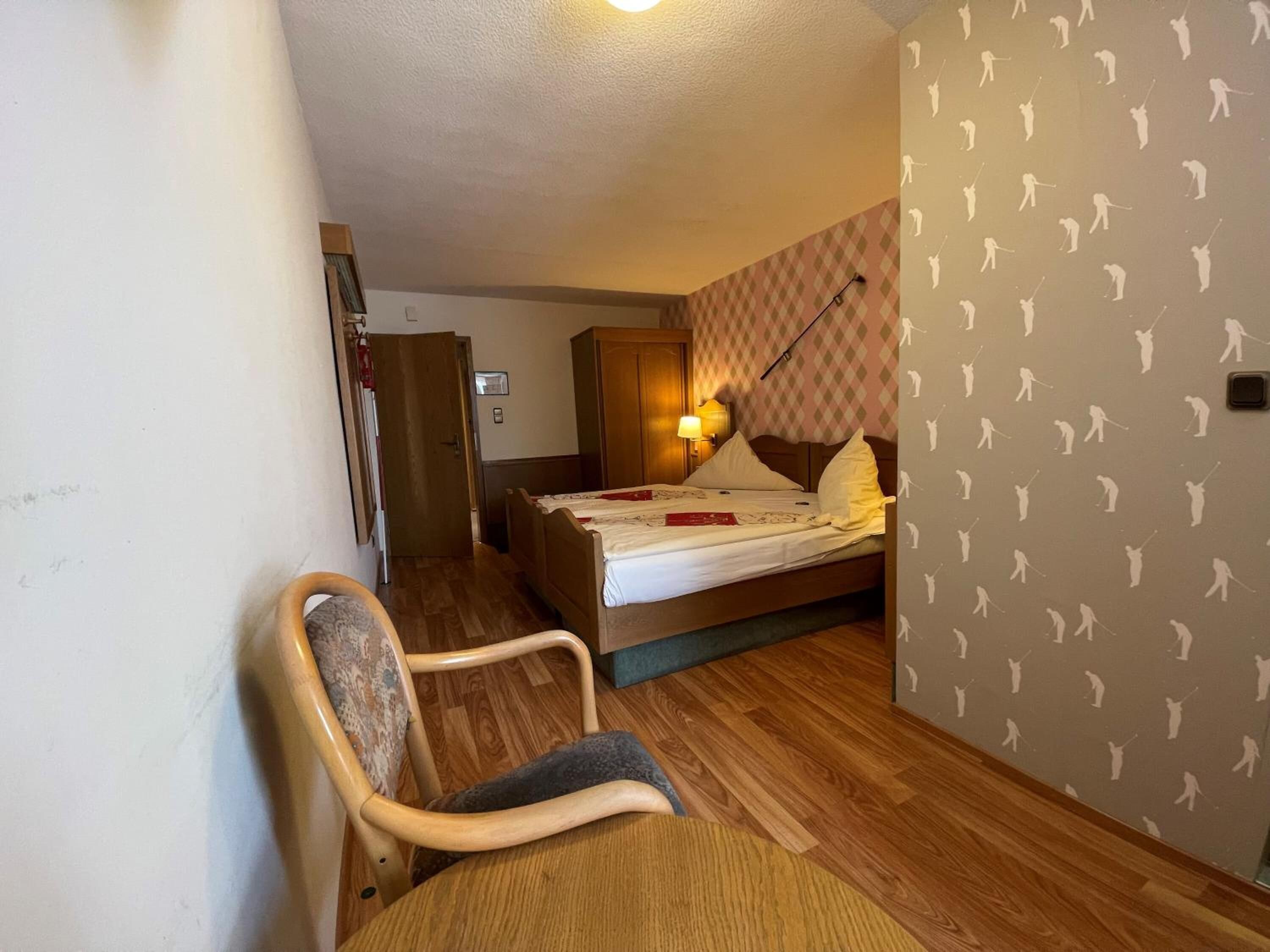 A bedroom with a bed, a chair, a wardrobe, and a wall with a pattern of figures.