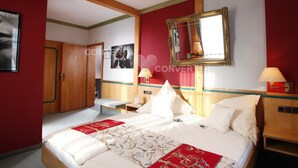 A hotel room with a large bed, wooden ceiling beams, a red accent wall, and a mirror above the bed. - Bebras Hessischer Hof (Bebra)