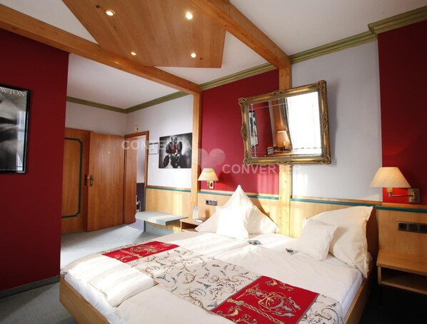 Una habitación de hotel con una cama grande, vigas de madera en el techo y una pared de acento roja, además de un espejo sobre la cama.