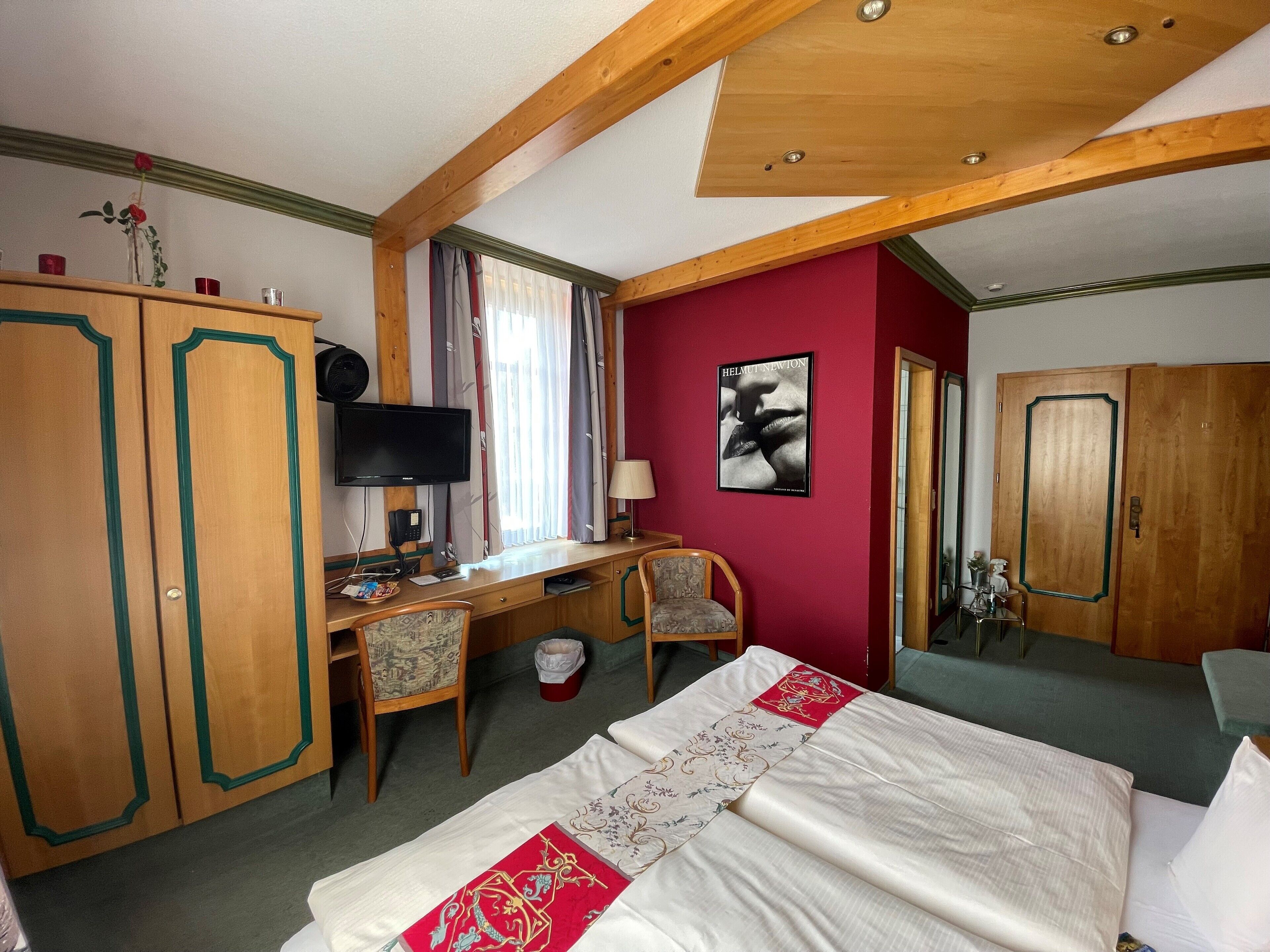 Ein Hotelzimmer mit Bett, Schreibtisch, Stuhl, Kleiderschrank und Fernseher.