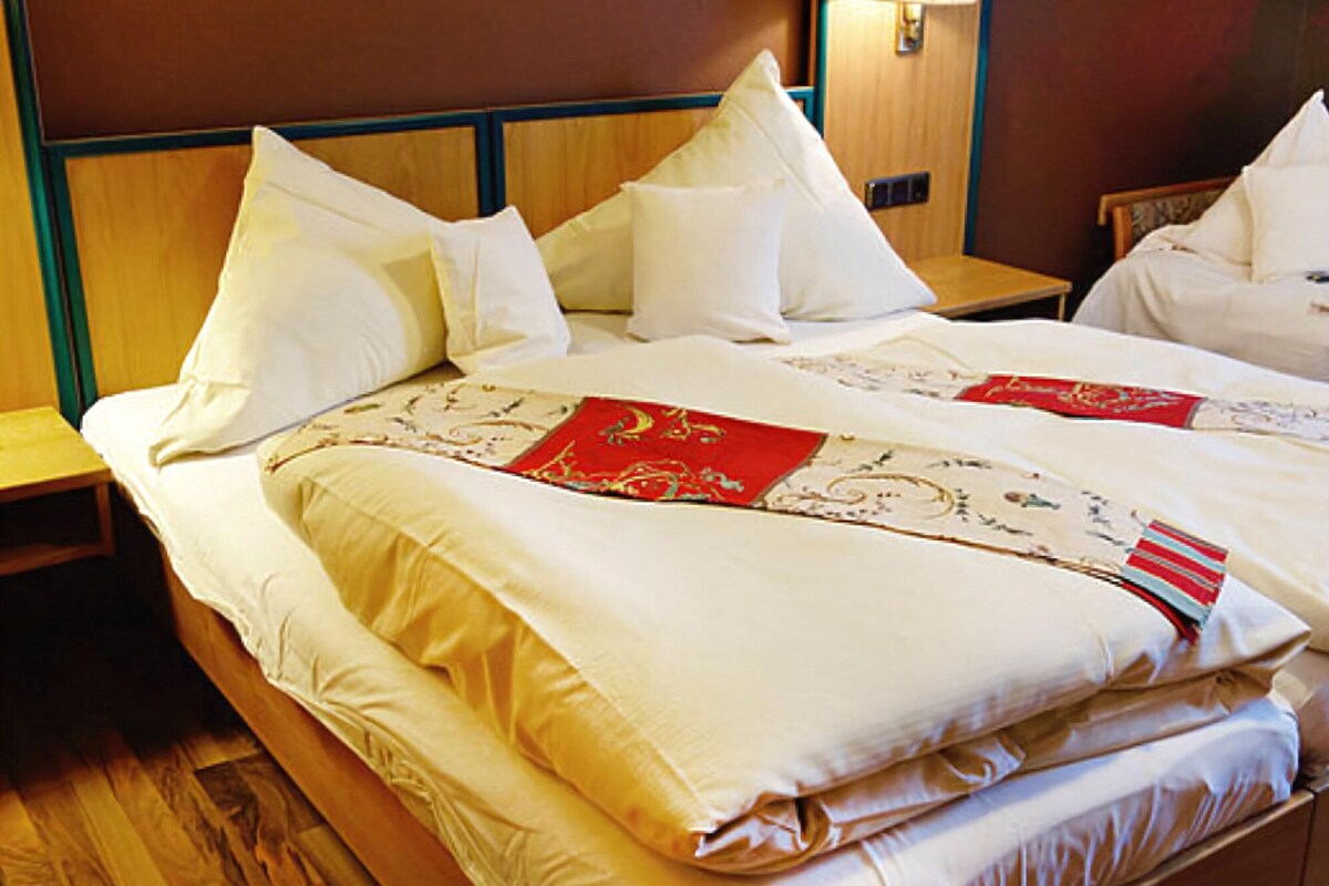 A hotel room with a large bed, multiple pillows, a wooden headboard, and a nightstand with a lamp.