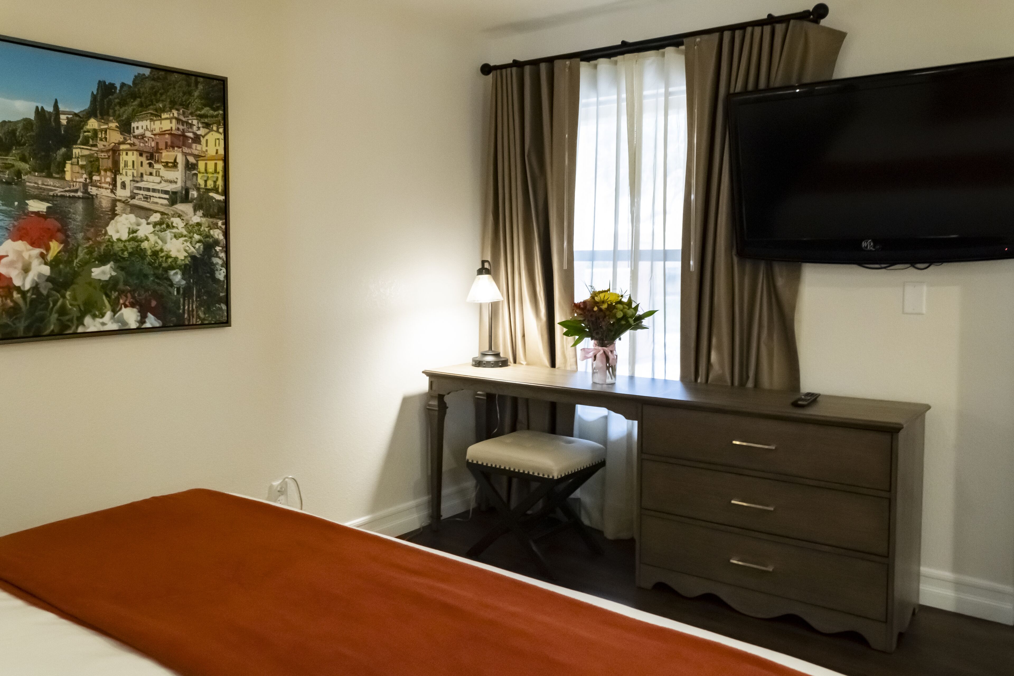 Een hotelkamer met een bed, een bureau met een stoel, een televisie en een schilderij van een kustplaats.